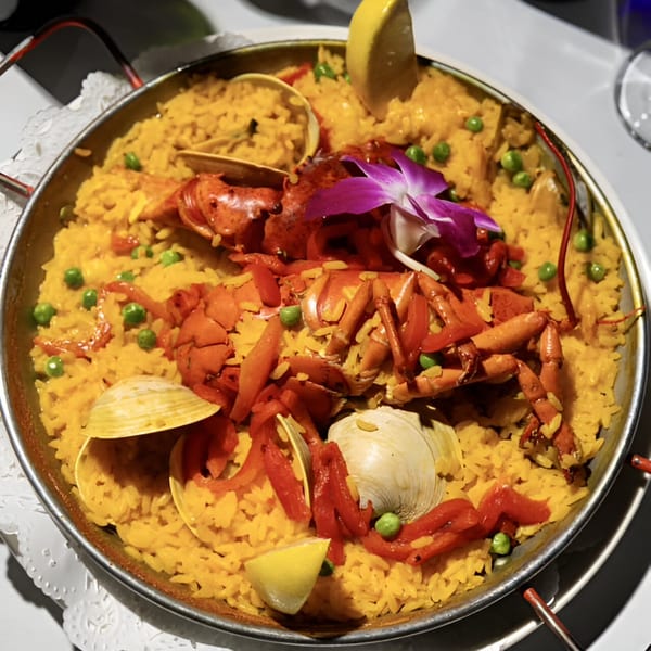 Portuguese seafood paella with lobster, clams, red peppers, peas, and lemon in a metal pan.