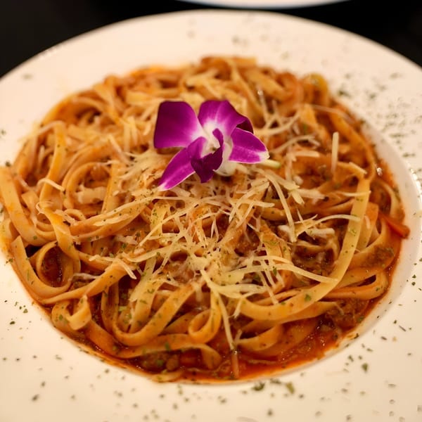 Fettuccine pasta with red sauce, shredded cheese, and a purple orchid on a white plate.