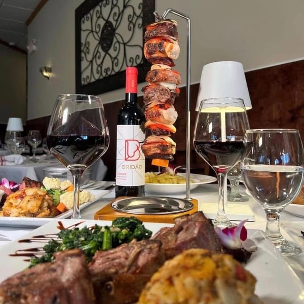 Portuguese steakhouse table with wine, hanging meat skewer, and various dishes.