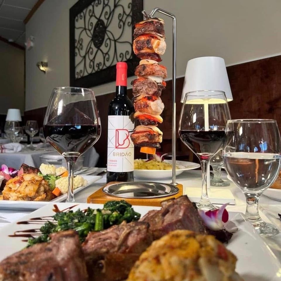 Portuguese steakhouse table with wine, hanging meat skewer, and various dishes.