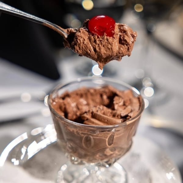 A spoonful of chocolate mousse with a cherry on top, held above a glass of mousse.