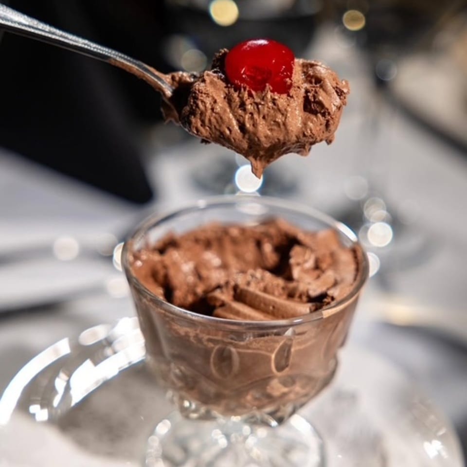 A spoonful of chocolate mousse with a cherry on top, held above a glass of mousse.